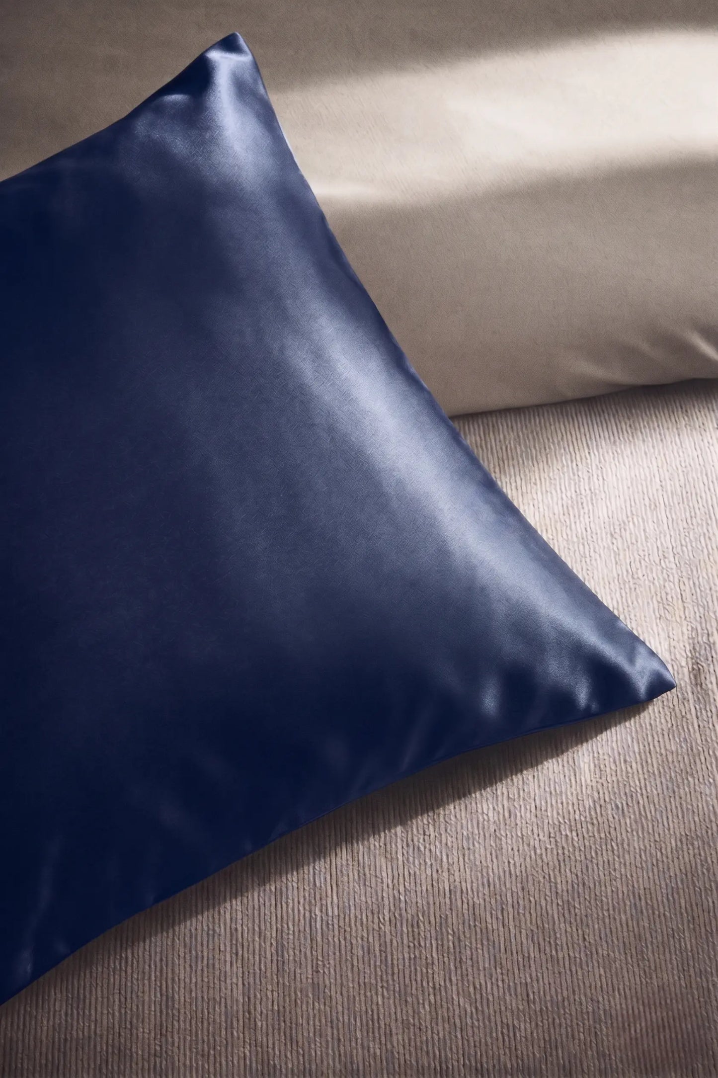 Taie d'oreiller en soie 19 mommes bleu marine sur coussin et fond beige pâle.