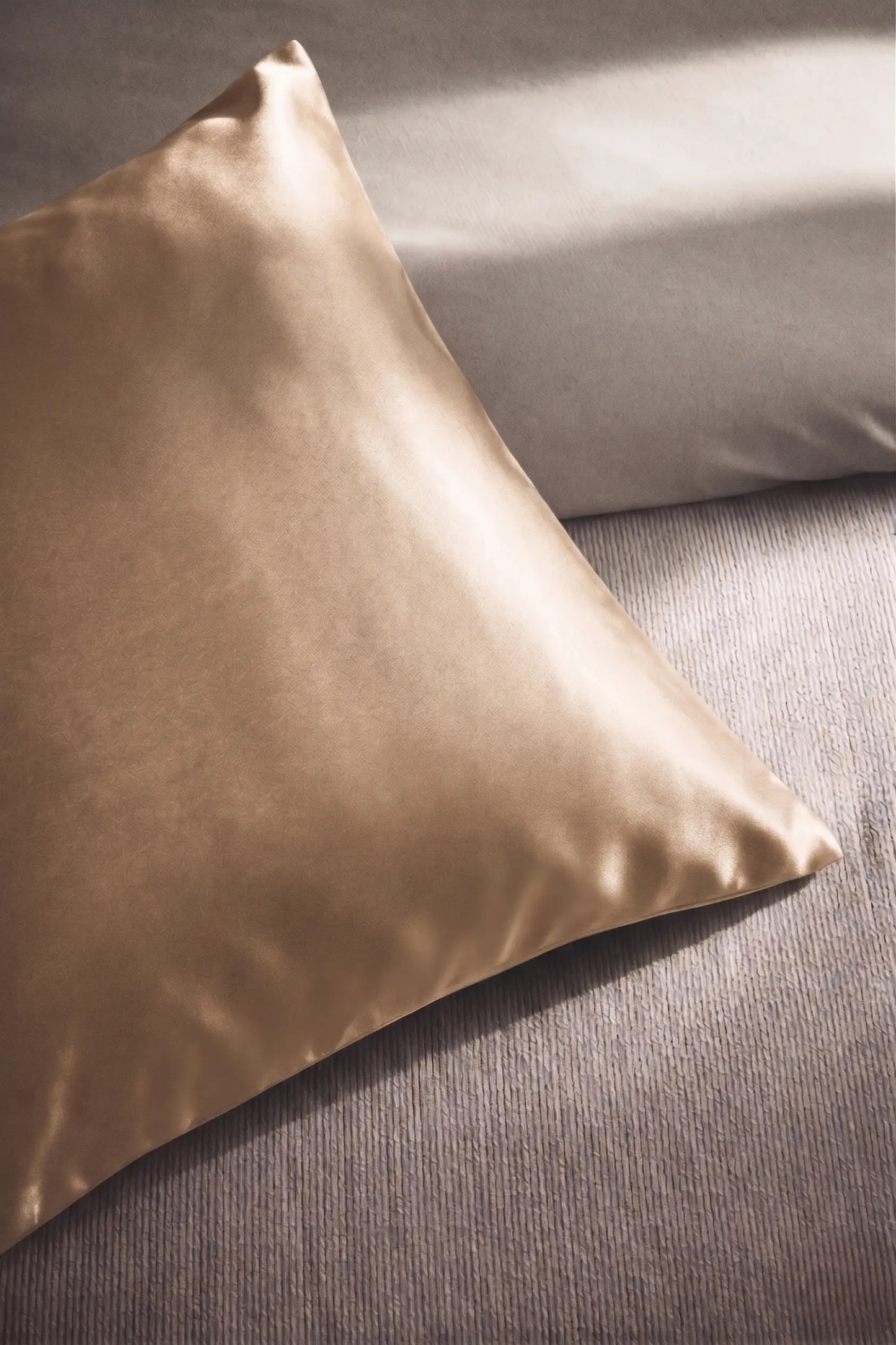 Taie d'oreiller en soie 19 mommes champagne sur coussin et fond beige pâle.
