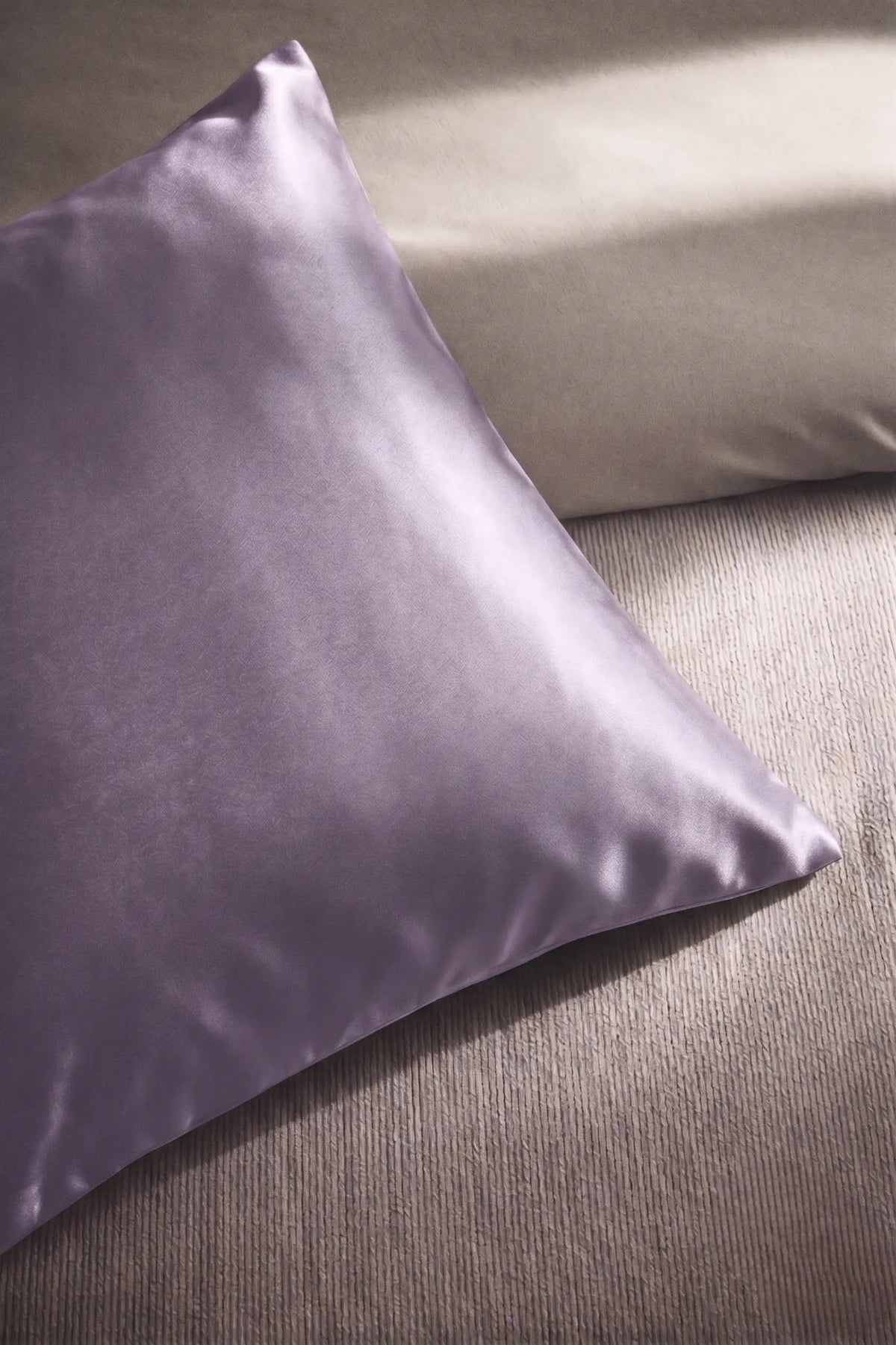 Taie d'oreiller en soie 19 mommes lavande sur coussin et fond beige pâle.