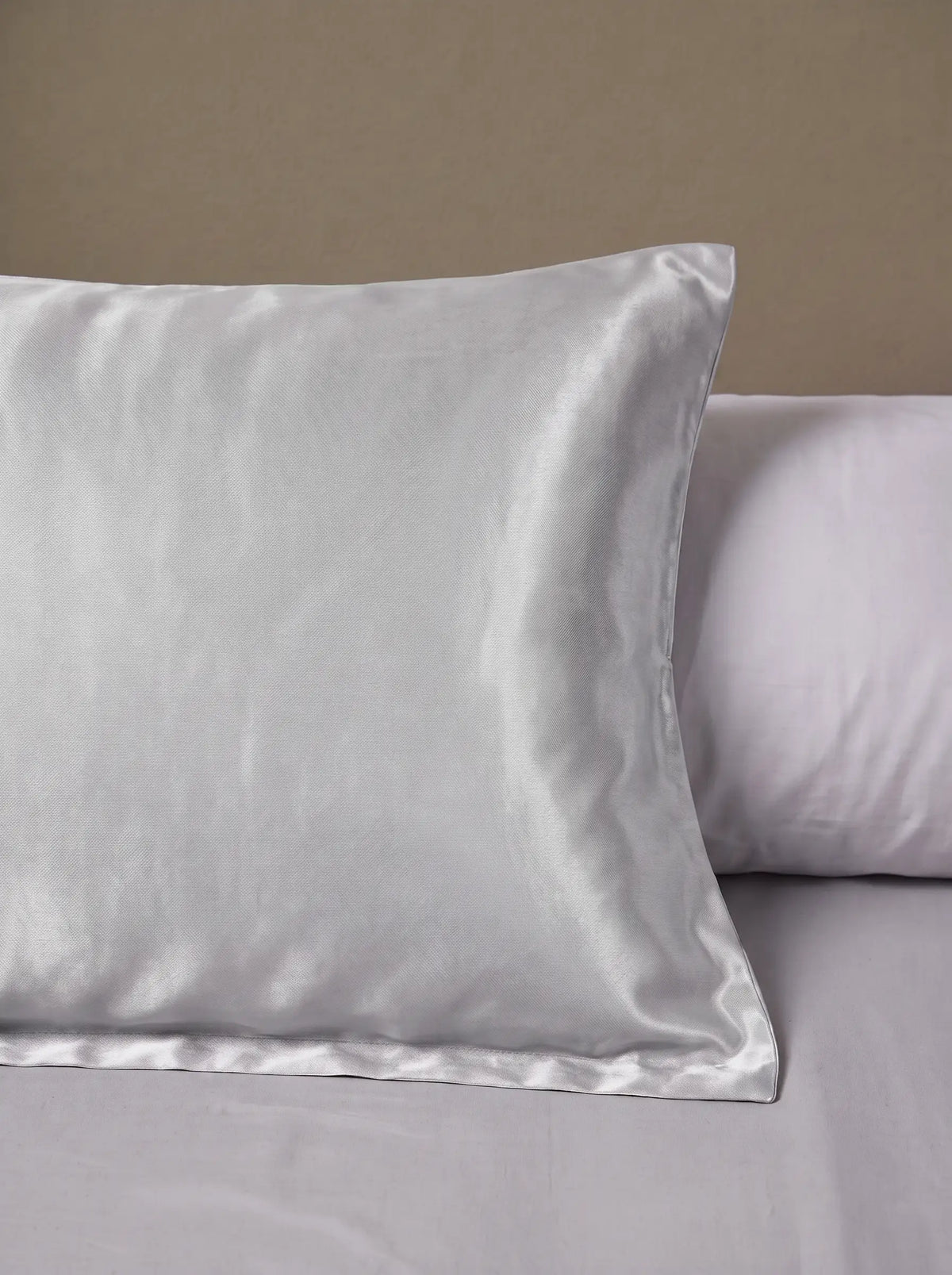 Taie d'oreiller en soie 25 mommes argenté posé sur un lit avec un oreiller blanc simple.