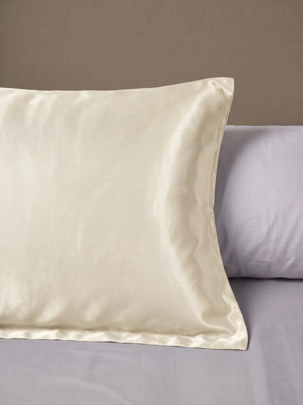 Taie d'oreiller en soie 25 mommes ivoire posé sur un lit avec un oreiller blanc simple.