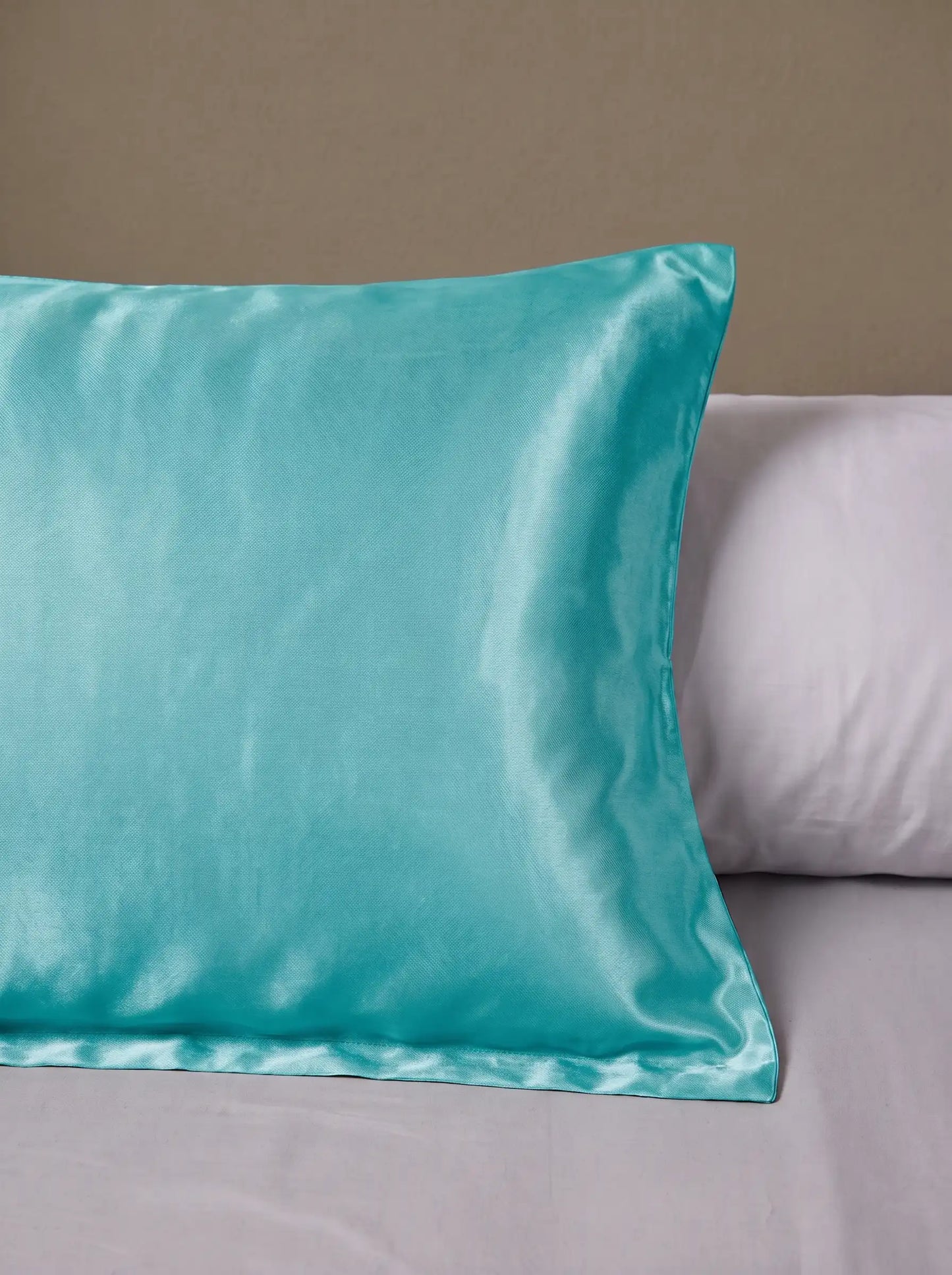 Taie d'oreiller en soie 25 mommes turquoise posé sur un lit avec un oreiller blanc simple.