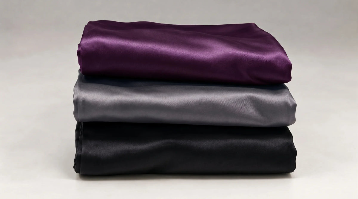 Trois taies d'oreiller en soie pliées et empilées, violet, gris et noir.