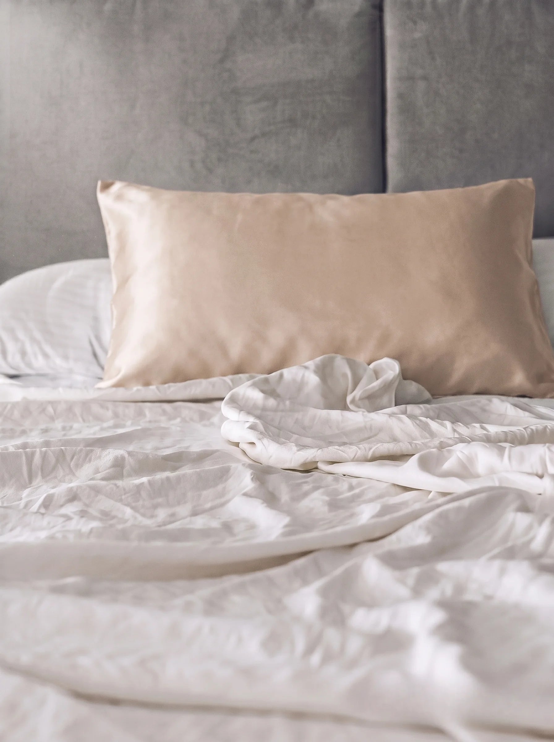 Taie d'oreiller en soie 19 mommes beige sur lit blanc avec fond gris.