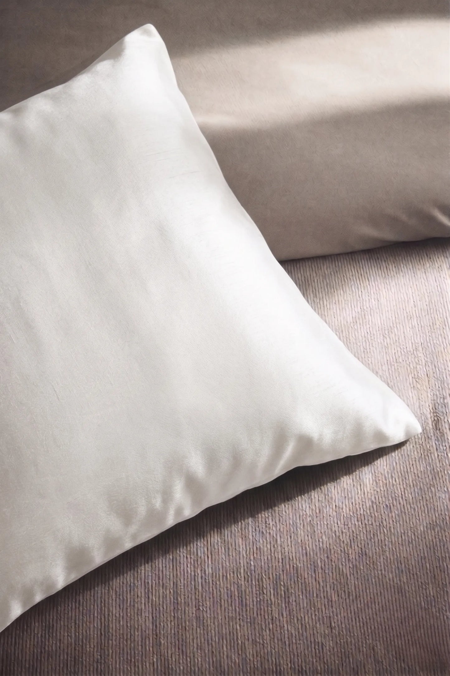 Taie d'oreiller en soie 19 mommes blanche sur coussin et fond beige pâle.