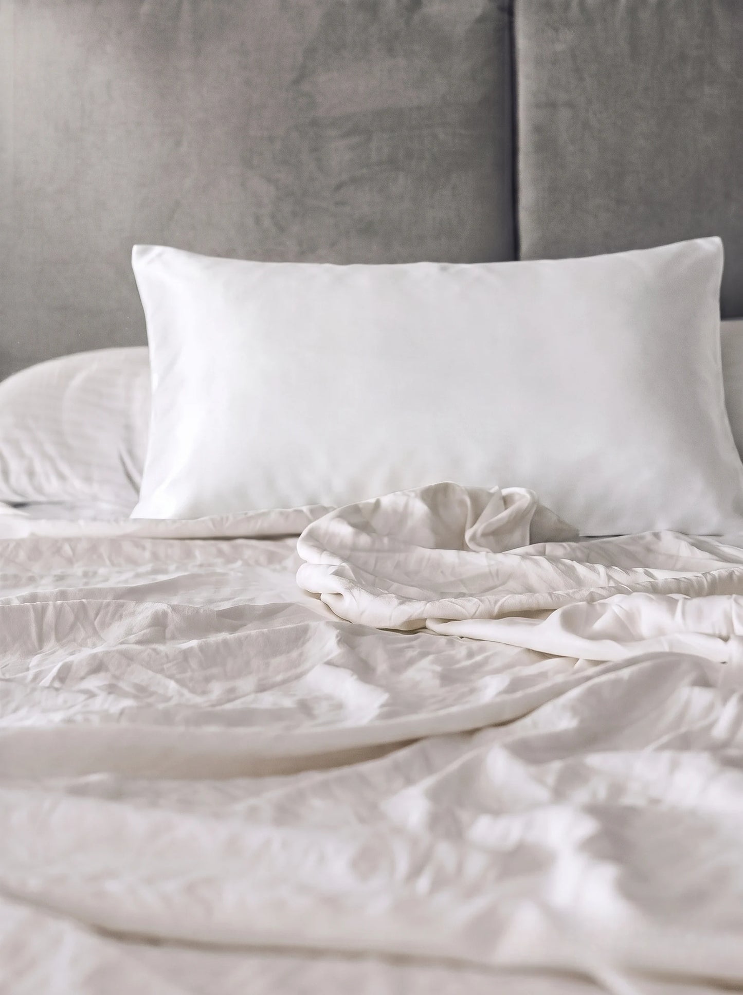 Taie d'oreiller en soie 19 mommes blanche sur lit blanc avec fond gris.