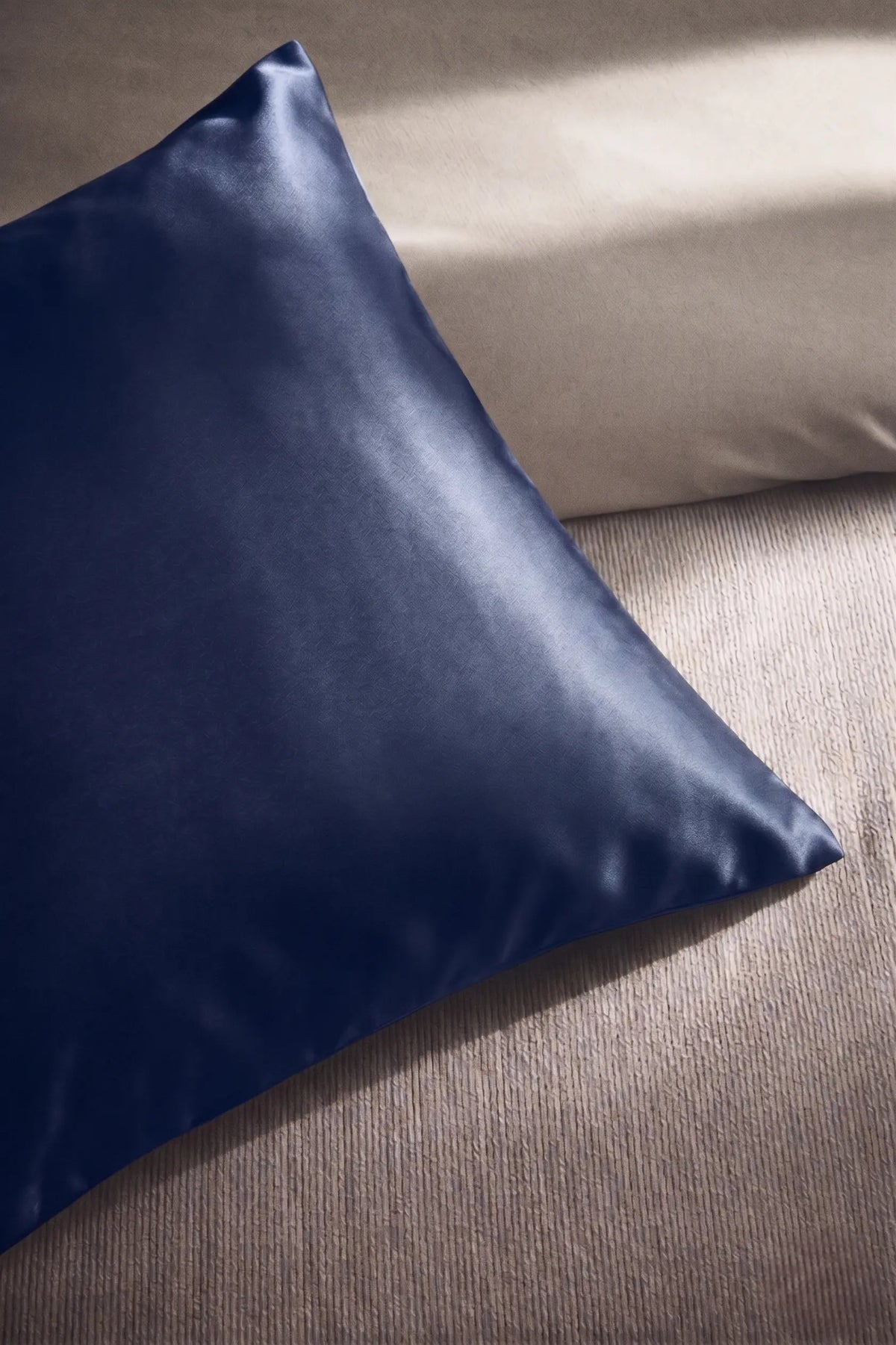 Taie d'oreiller en soie 19 mommes bleu marine sur coussin et fond beige pâle.