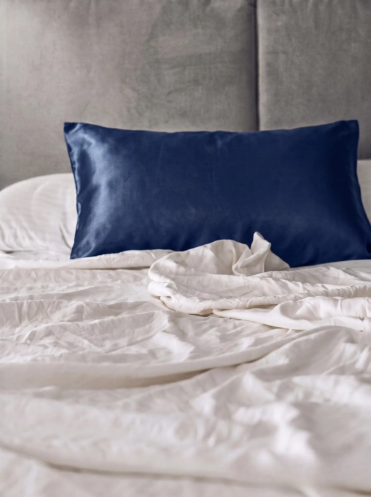 Taie d'oreiller en soie 19 mommes bleu marine sur lit blanc avec fond gris.