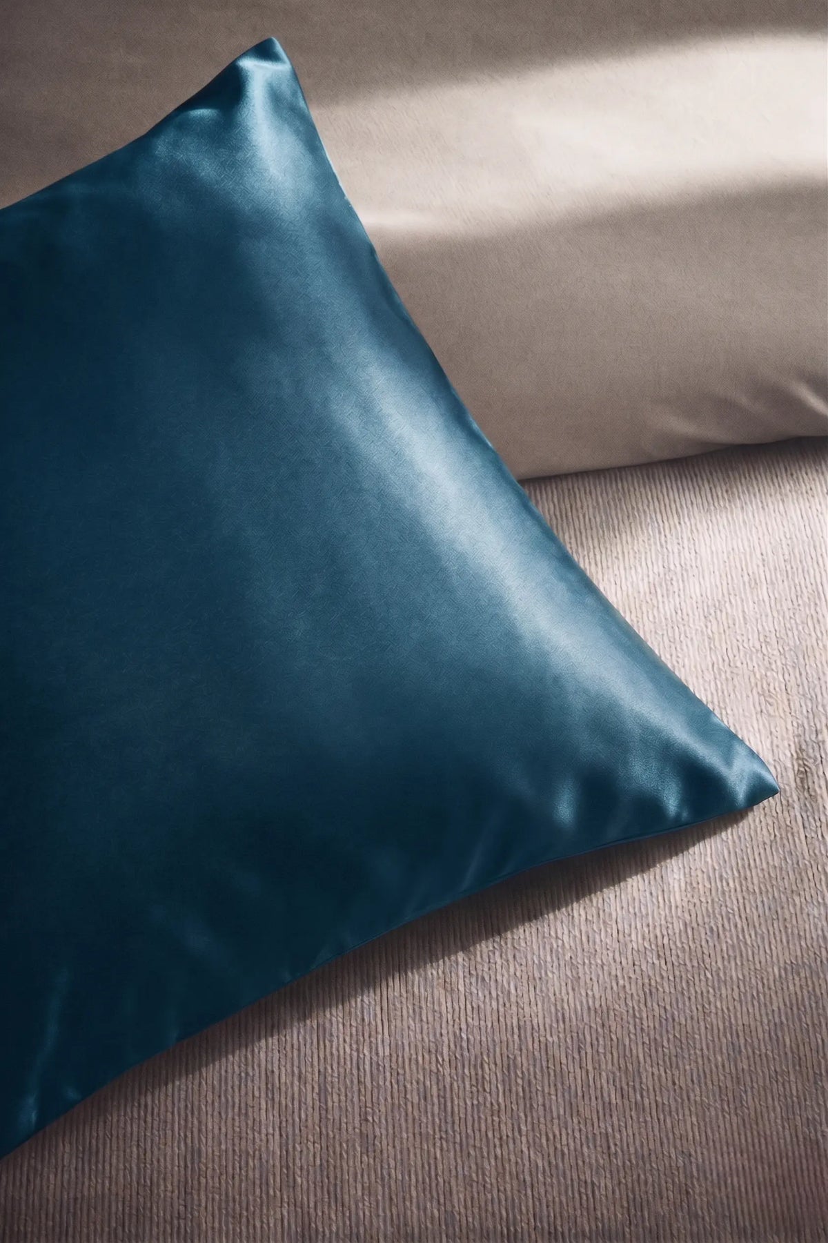 Taie d'oreiller en soie 19 mommes bleu paon sur coussin et fond beige pâle.