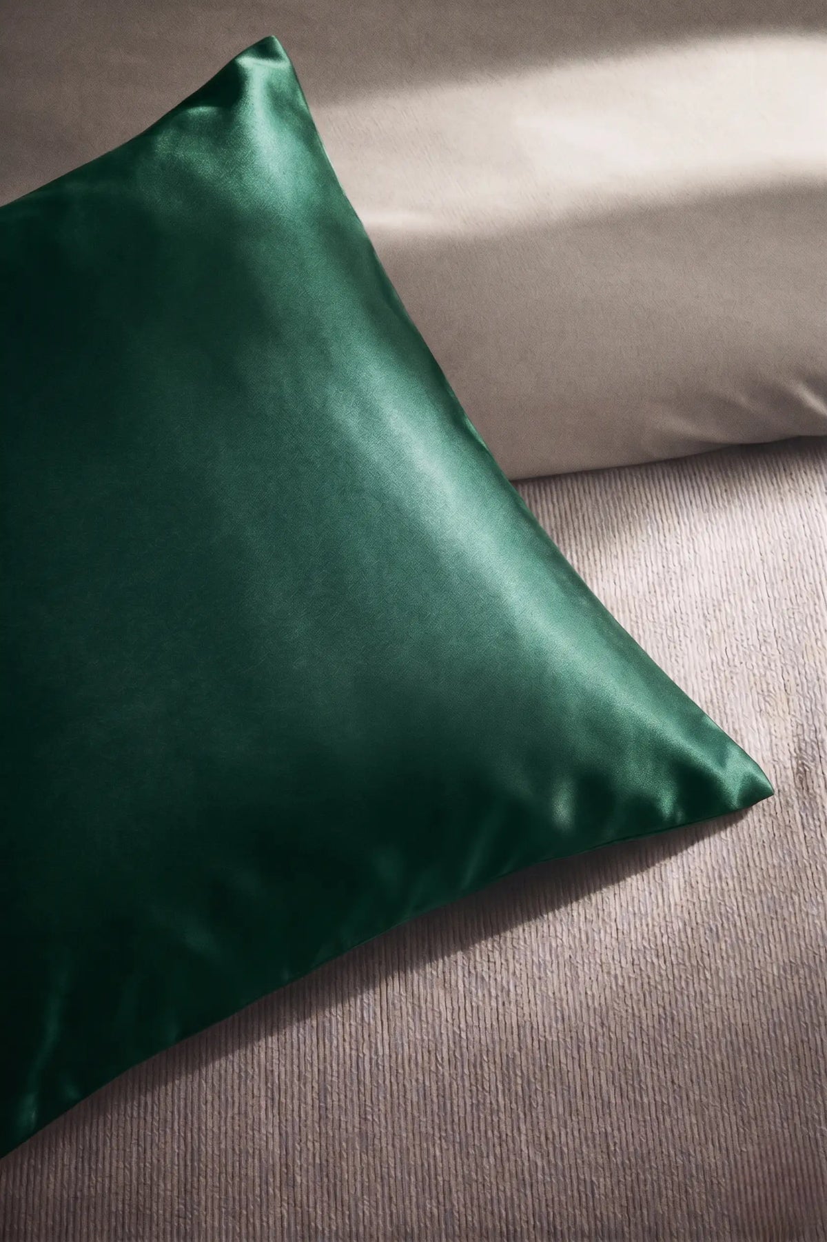 Taie d'oreiller en soie 19 mommes émeraude sur coussin et fond beige pâle.