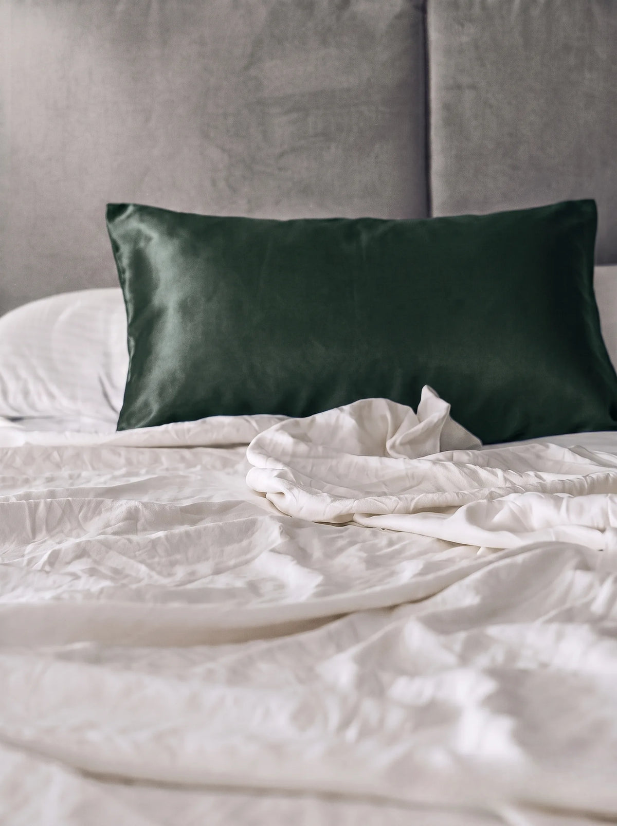 Taie d'oreiller en soie 19 mommes émeraude sur lit blanc avec fond gris.