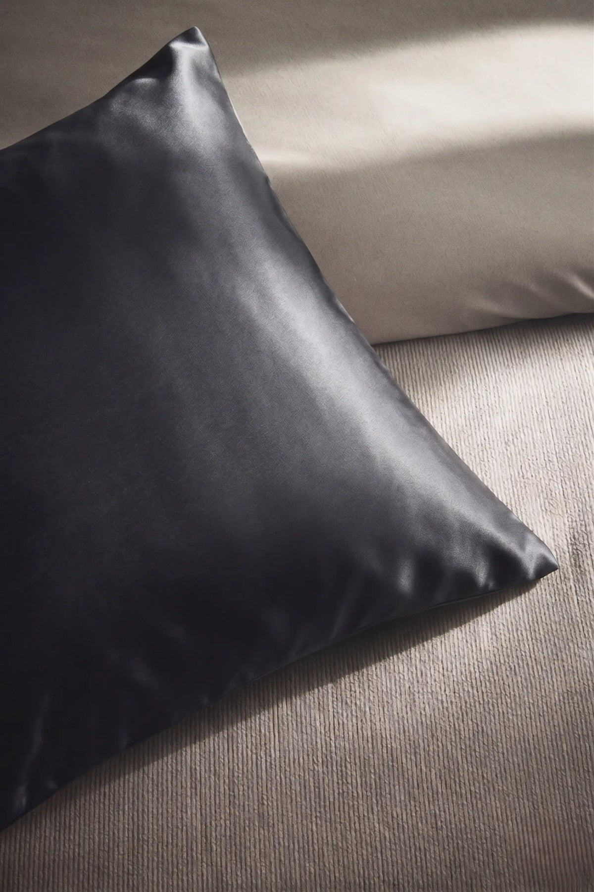 Taie d'oreiller en soie 19 mommes grise foncée sur coussin et fond beige pâle.