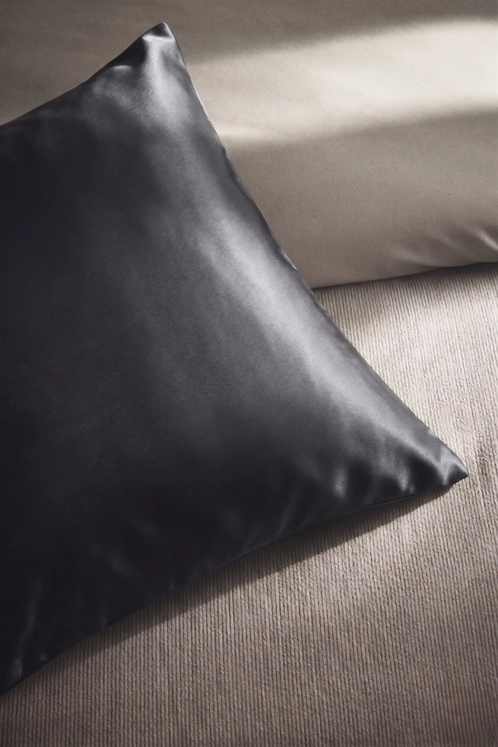 Taie d'oreiller en soie 19 mommes grise foncée sur coussin et fond beige pâle.