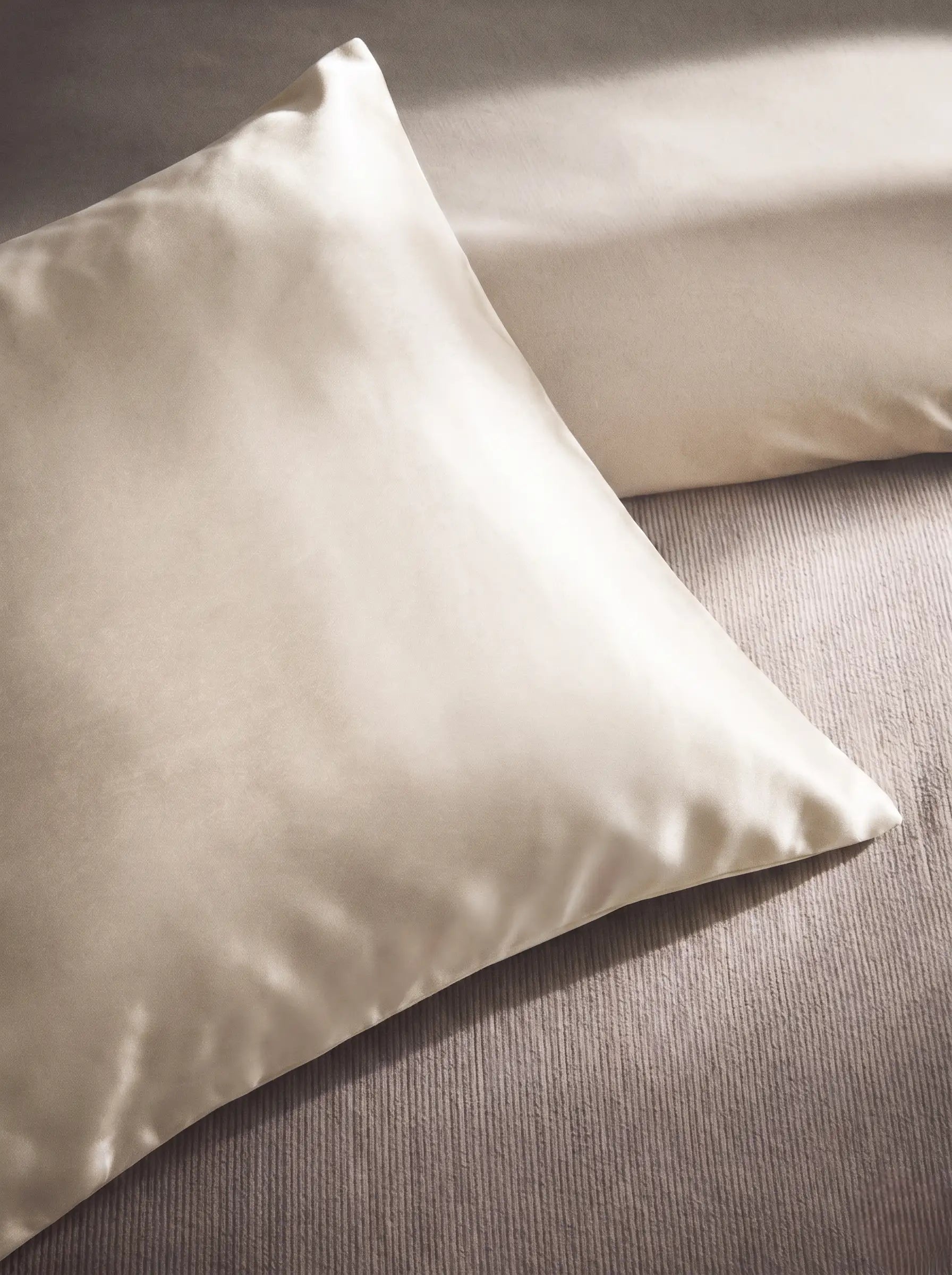 Taie d'oreiller en soie 19 mommes ivoire sur coussin et fond beige pâle.