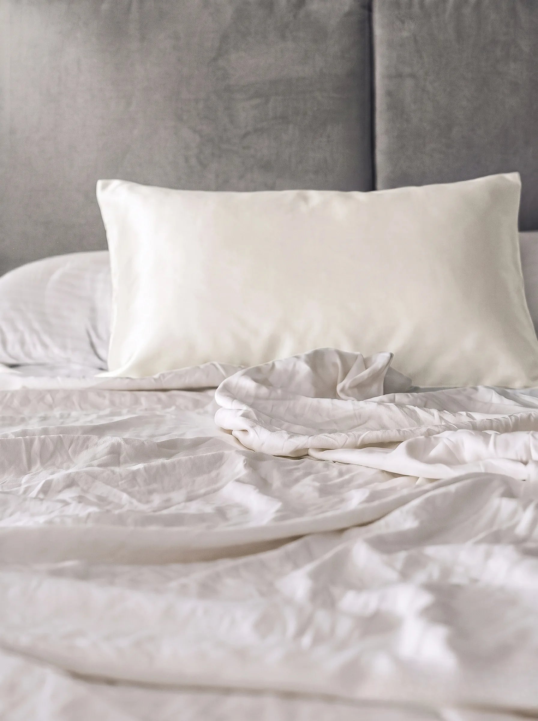 Taie d'oreiller en soie 19 mommes ivoire sur lit blanc avec fond gris.