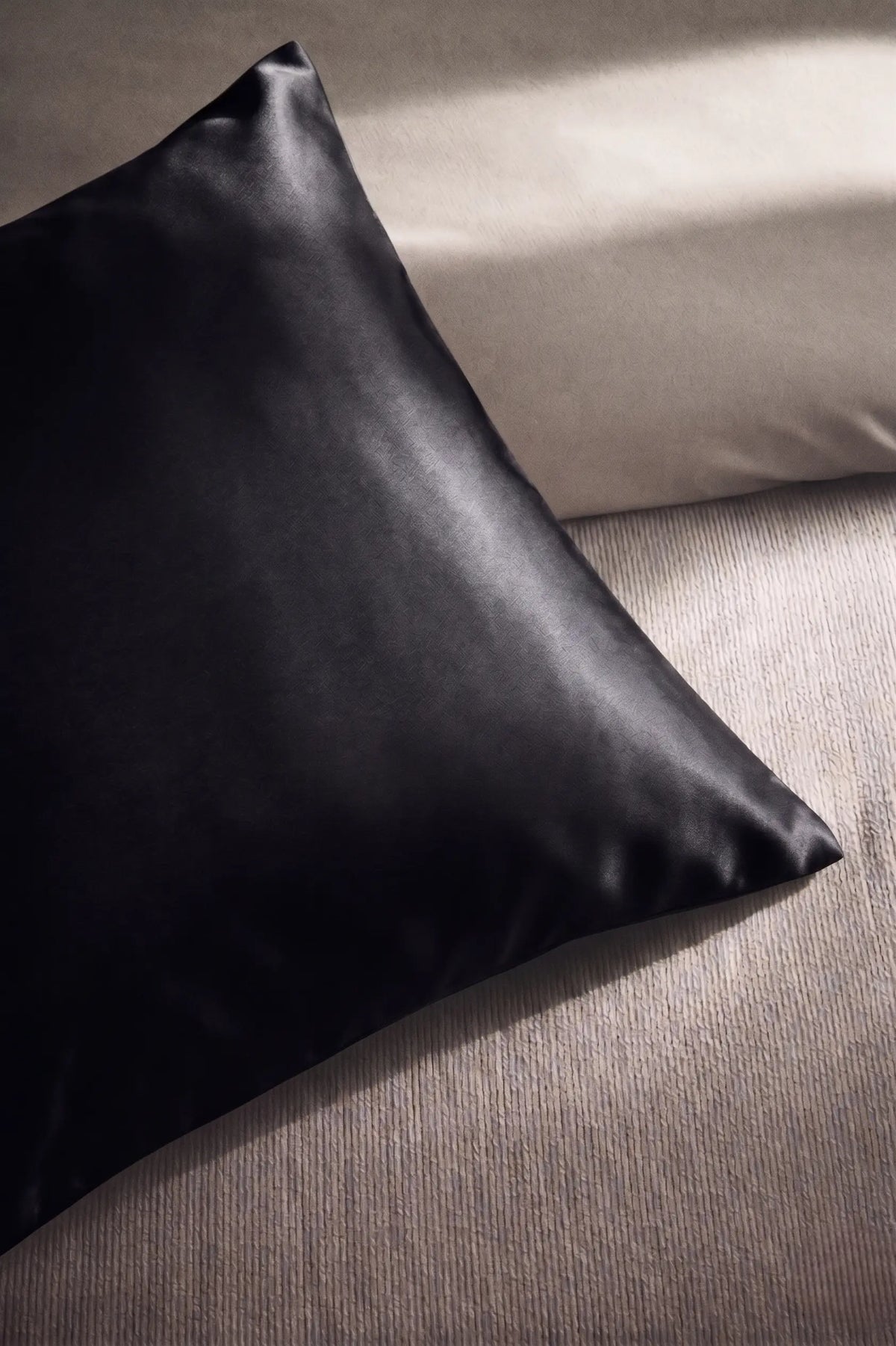 Taie d'oreiller en soie 19 mommes noir sur coussin et fond beige pâle.