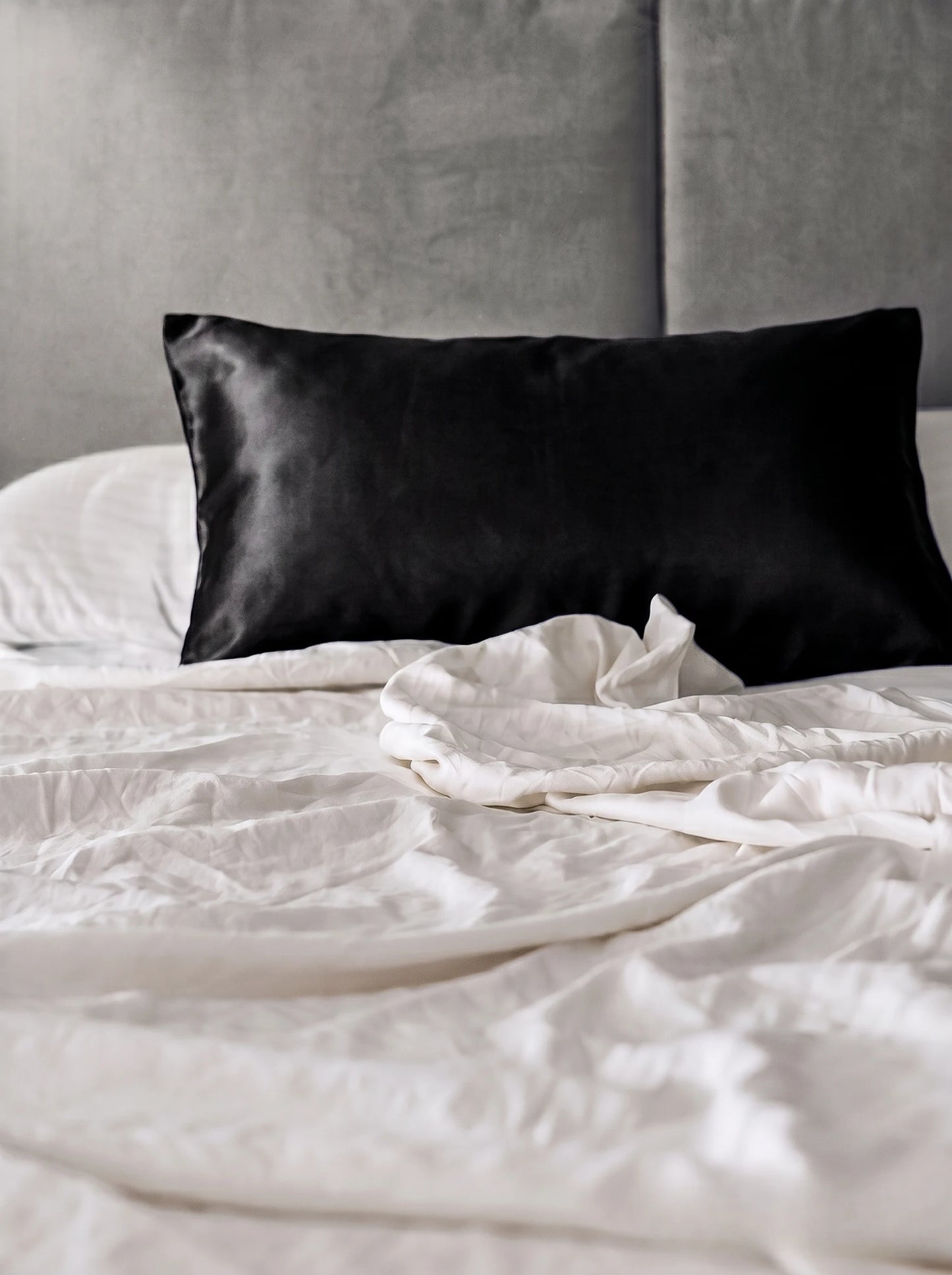 Taie d'oreiller en soie 19 mommes noire sur lit blanc avec fond gris.