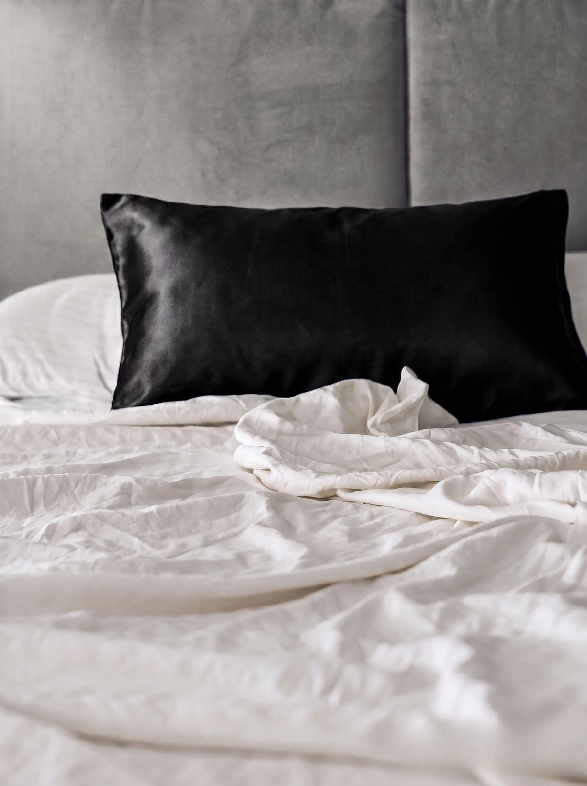 Taie d'oreiller en soie 19 mommes noire sur lit blanc avec fond gris.