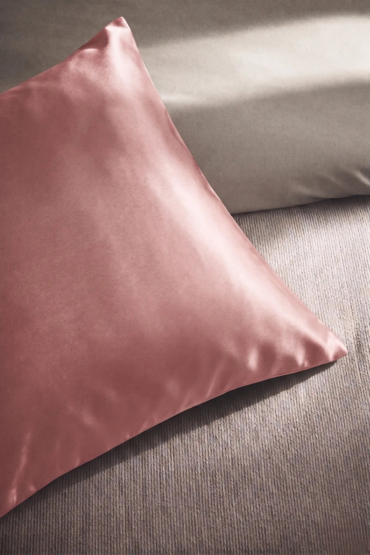 Taie d'oreiller en soie 19 mommes rose sur coussin et fond beige pâle.