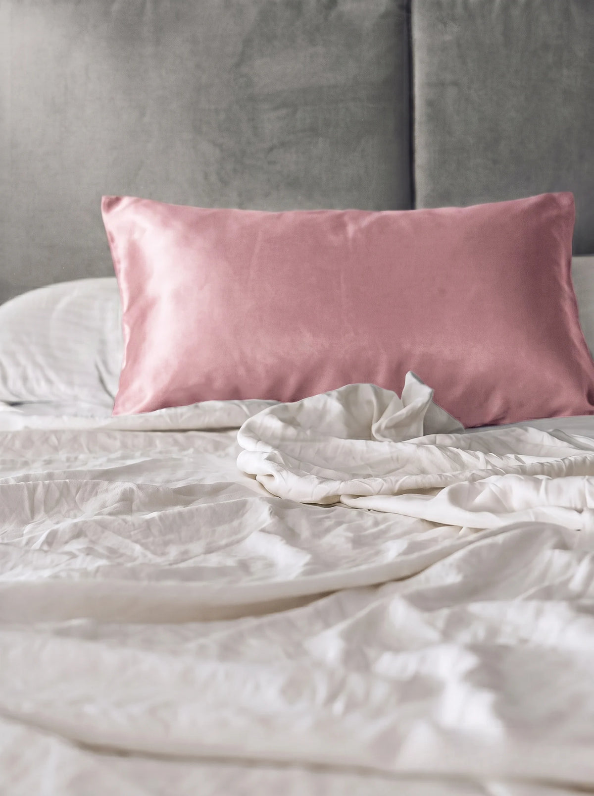 Taie d'oreiller en soie 19 mommes rose sur lit blanc avec fond gris.