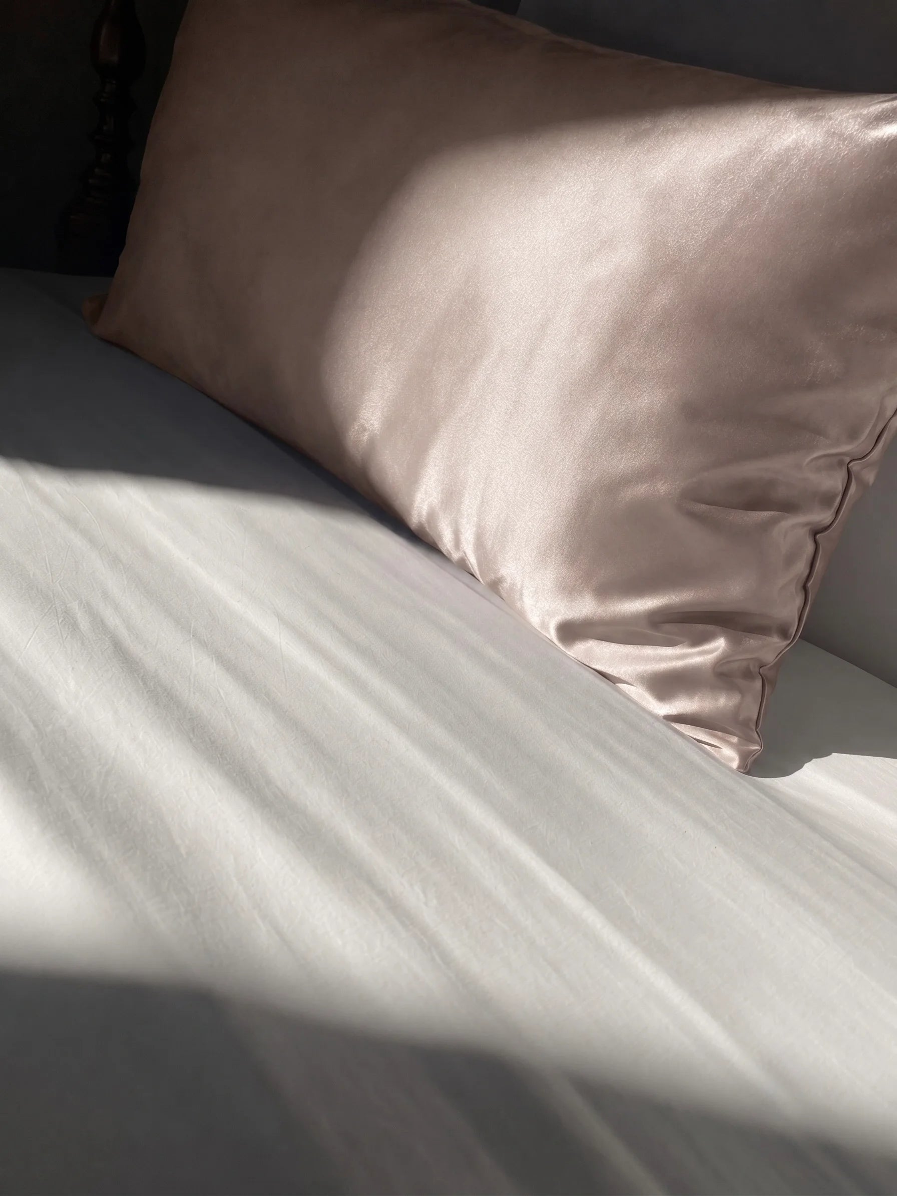 Taie d'oreiller en soie 22 mommes beige sur lit blanc.