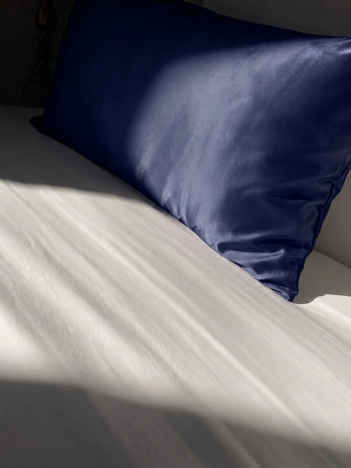 Taie d'oreiller en soie 22 mommes bleu marine sur lit blanc.