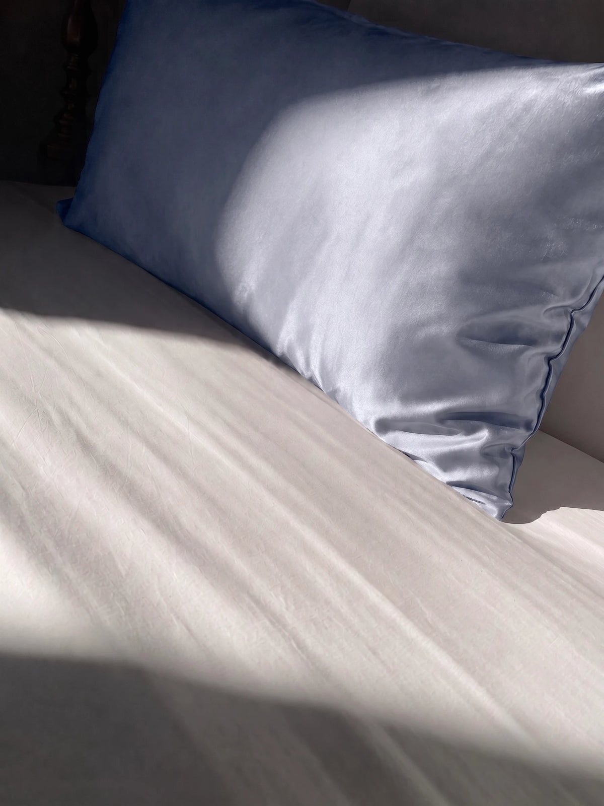 Taie d'oreiller en soie 22 mommes grise bleu sur lit blanc.