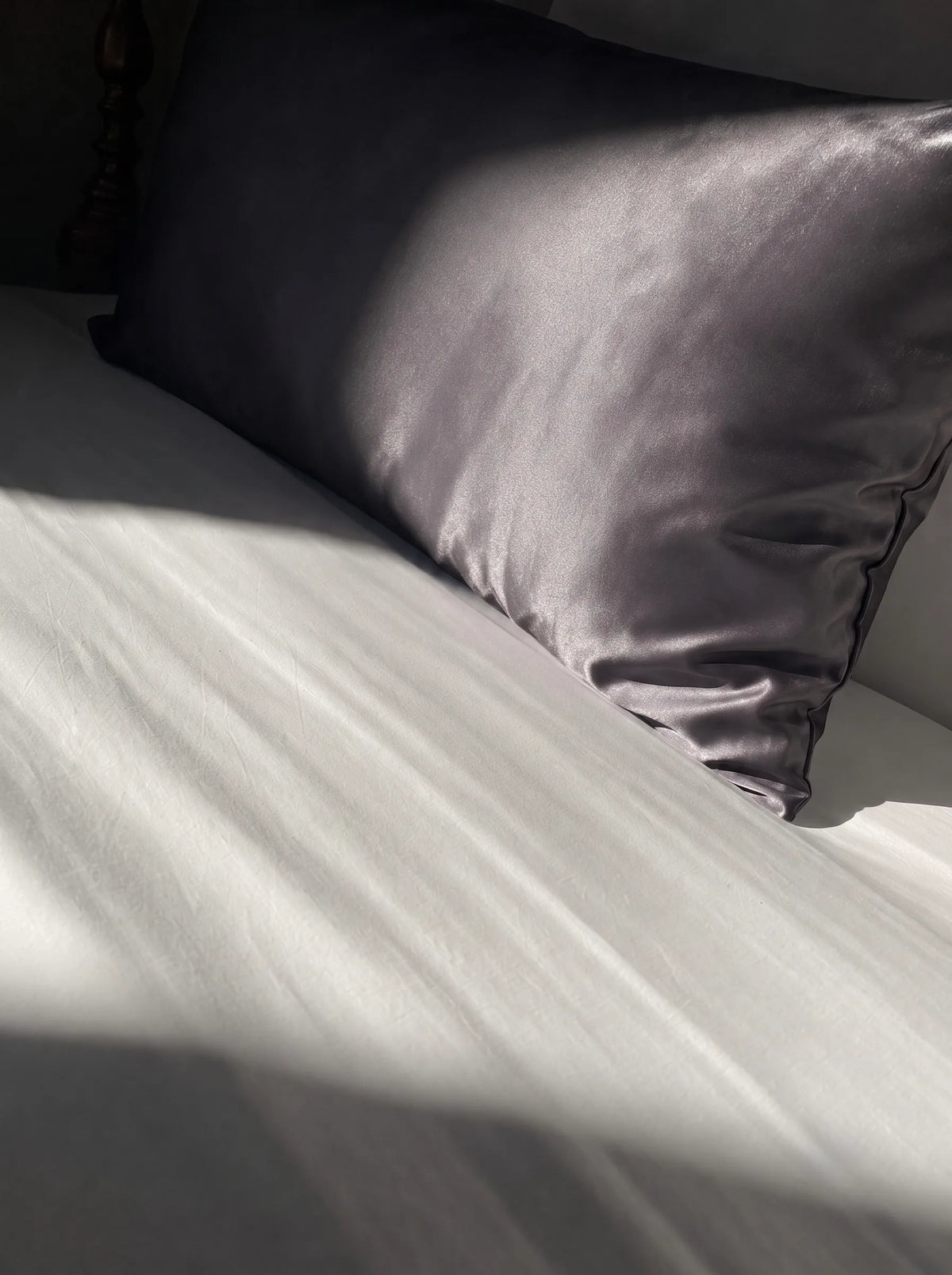 Taie d'oreiller en soie 22 mommes grise foncée sur lit blanc.