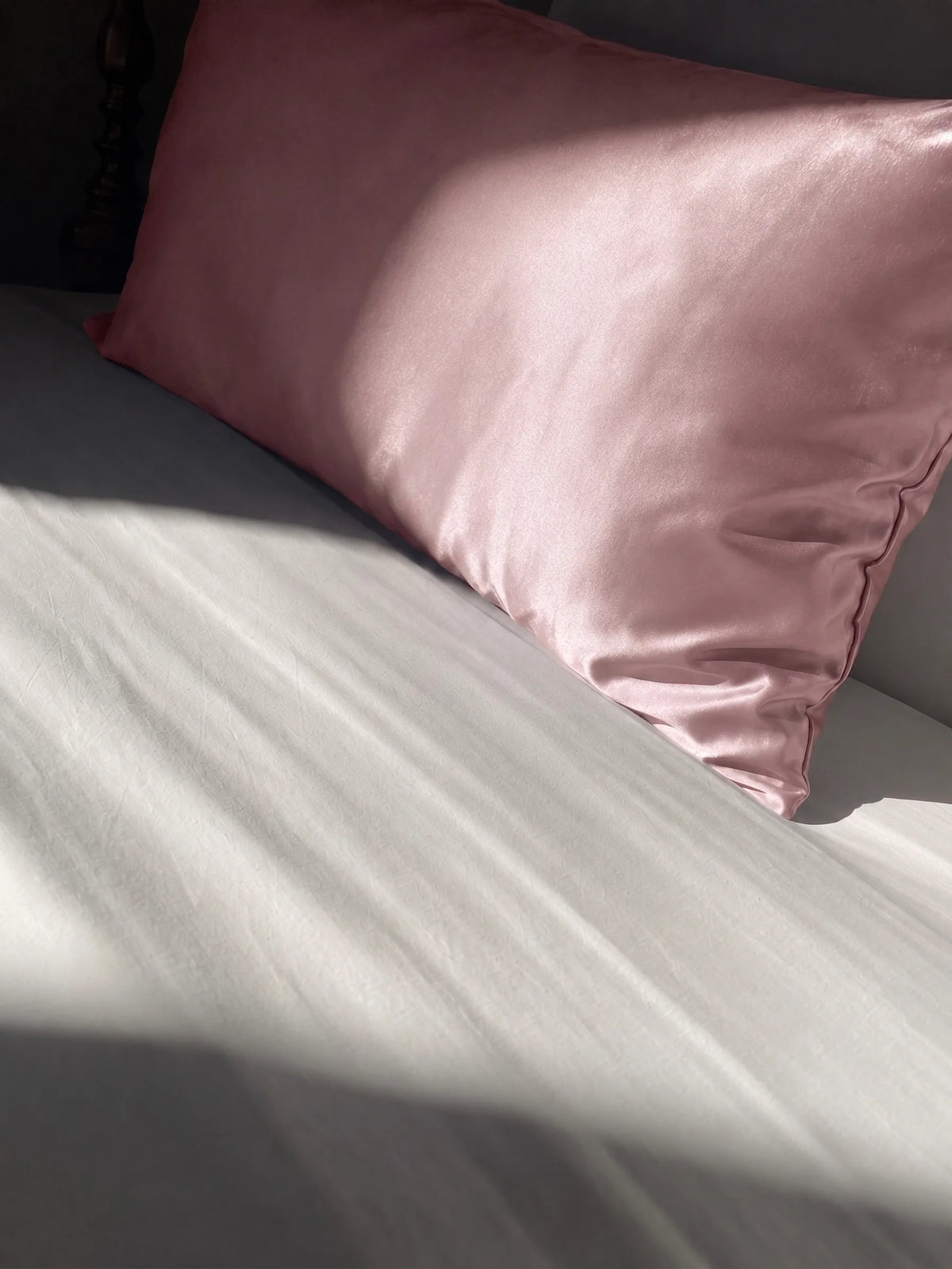 Taie d'oreiller en soie 22 mommes rose sur lit blanc.