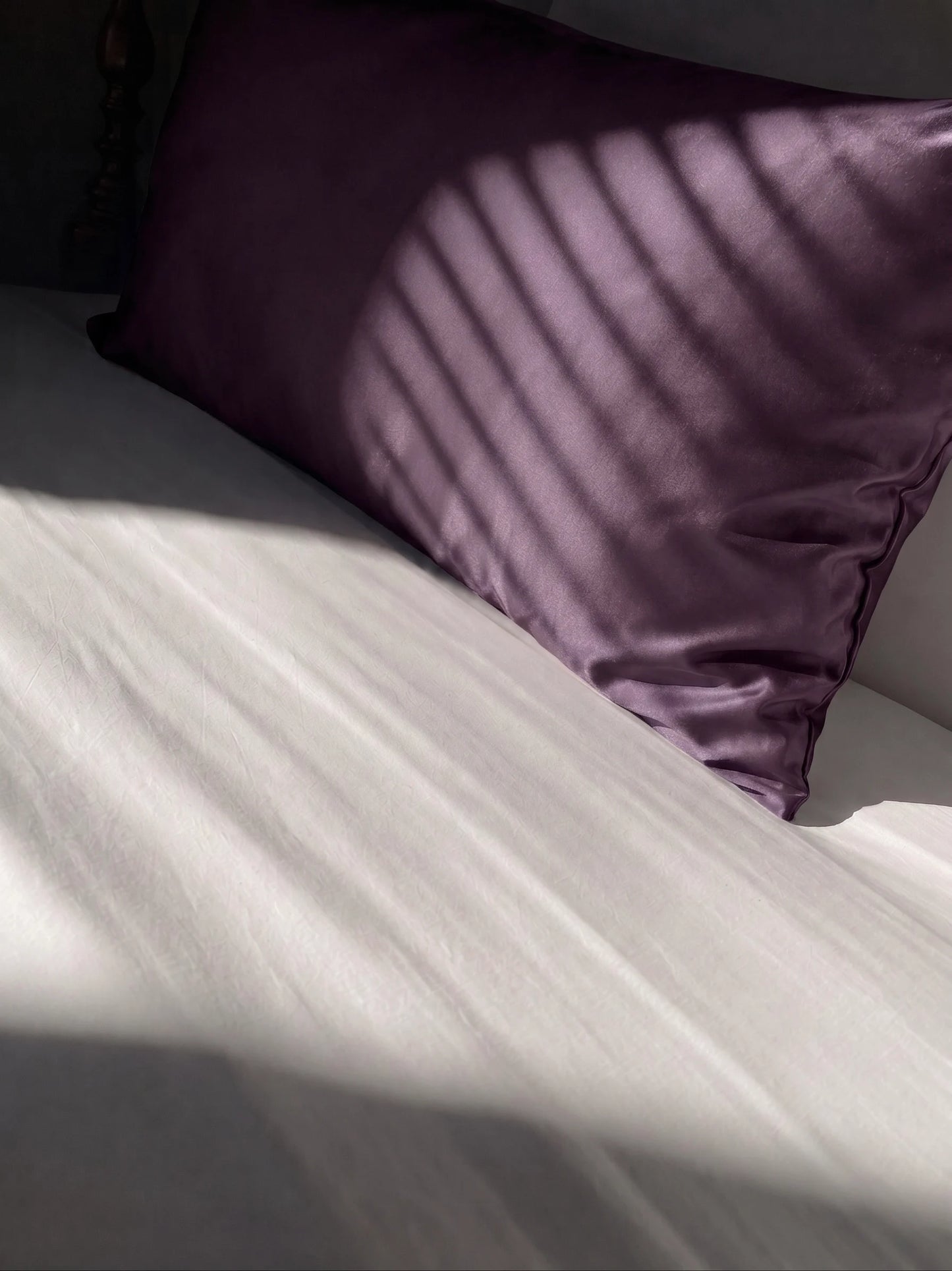 Taie d'oreiller en soie 22 mommes violette sur lit blanc.