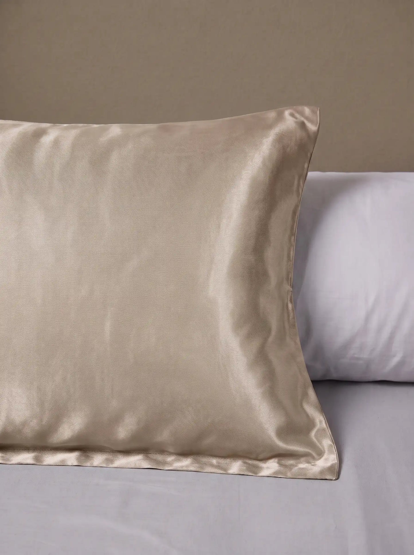 Taie d'oreiller en soie 25 mommes beige posé sur un lit avec un oreiller blanc simple.
