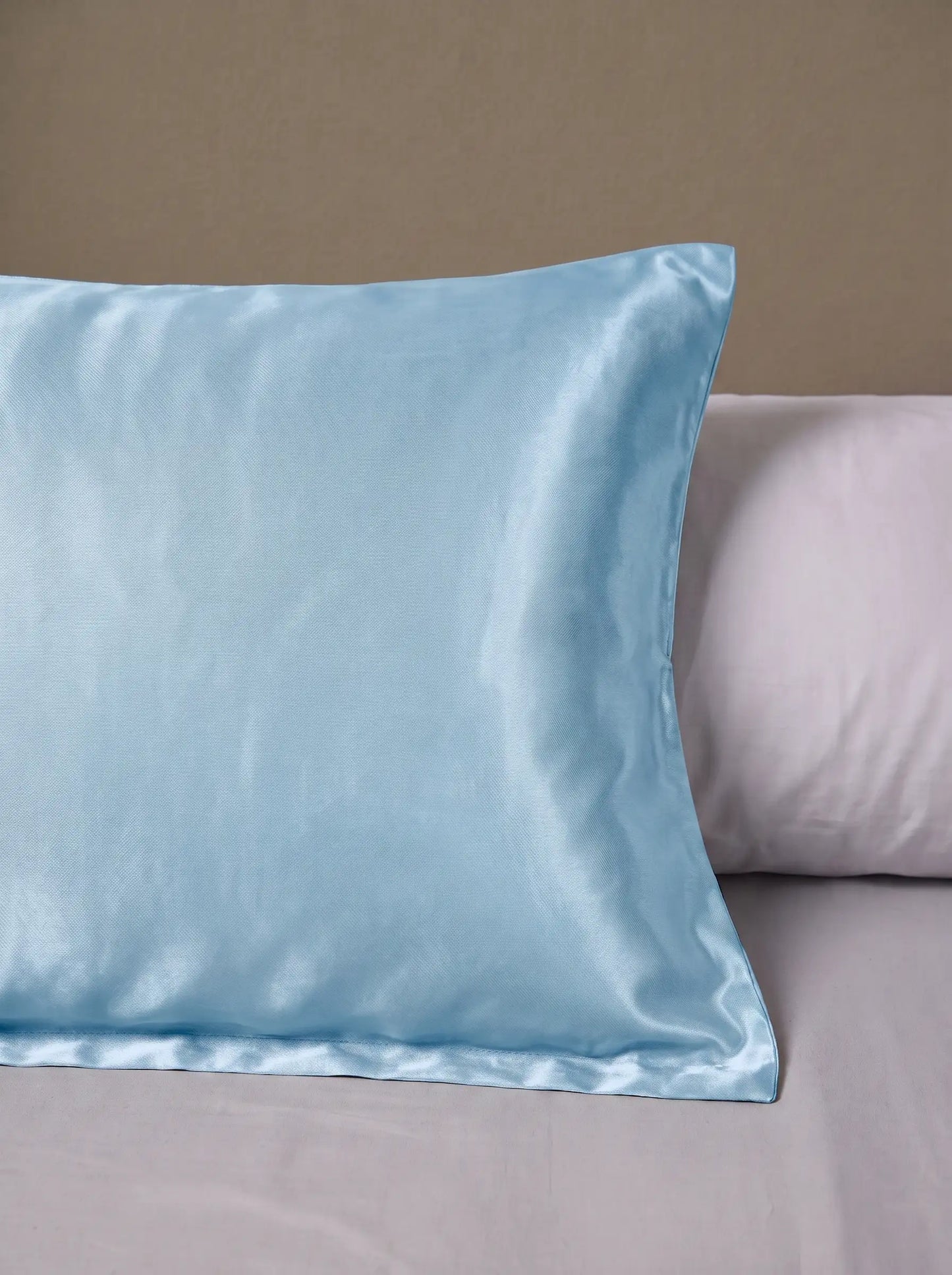 Taie d'oreiller en soie 25 mommes bleu ciel posé sur un lit avec un oreiller blanc simple.