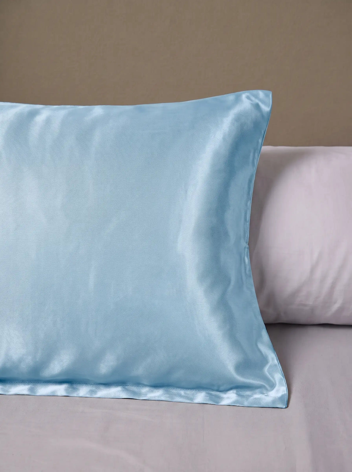 Taie d'oreiller en soie 25 mommes bleu ciel posé sur un lit avec un oreiller blanc simple.