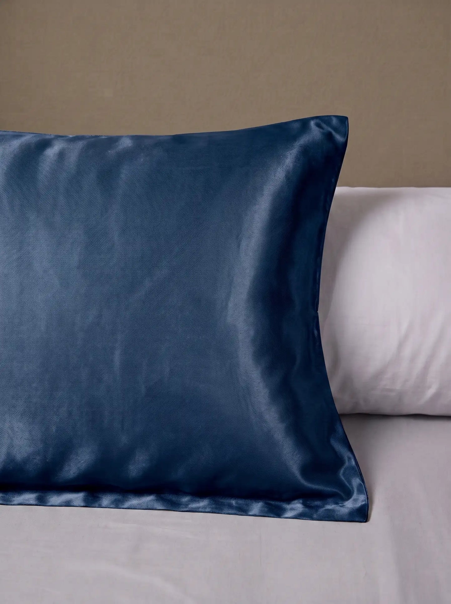 Taie d'oreiller en soie 25 mommes bleu marine posé sur un lit avec un oreiller blanc simple.