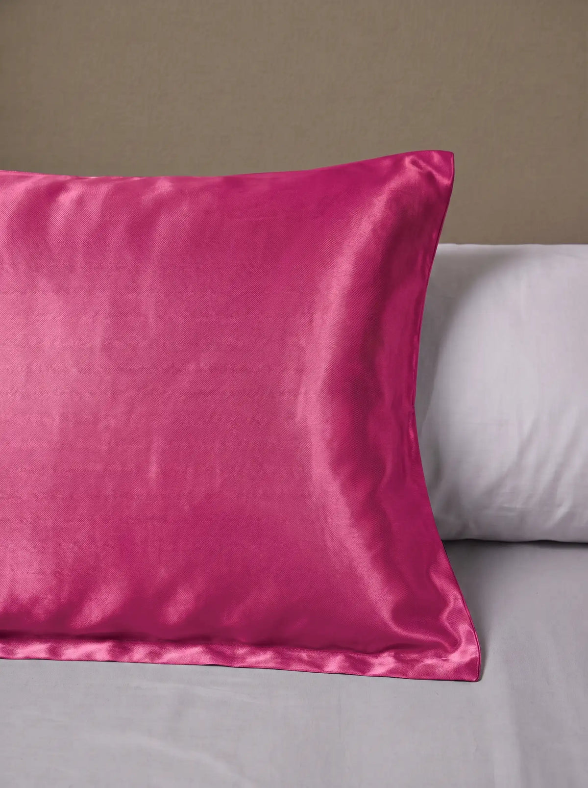 Taie d'oreiller en soie 25 mommes fuchsia posé sur un lit avec un oreiller blanc simple.