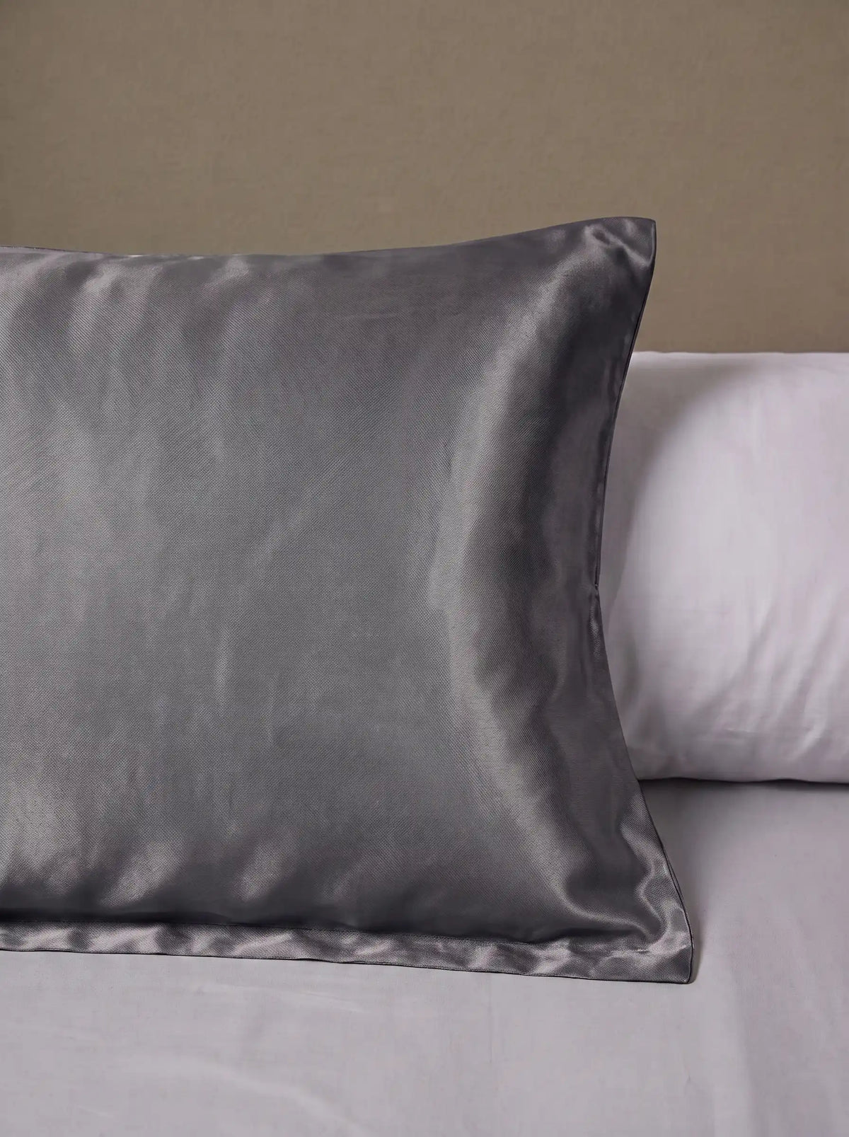 Taie d'oreiller en soie 25 mommes grise foncée posé sur un lit avec un oreiller blanc simple.