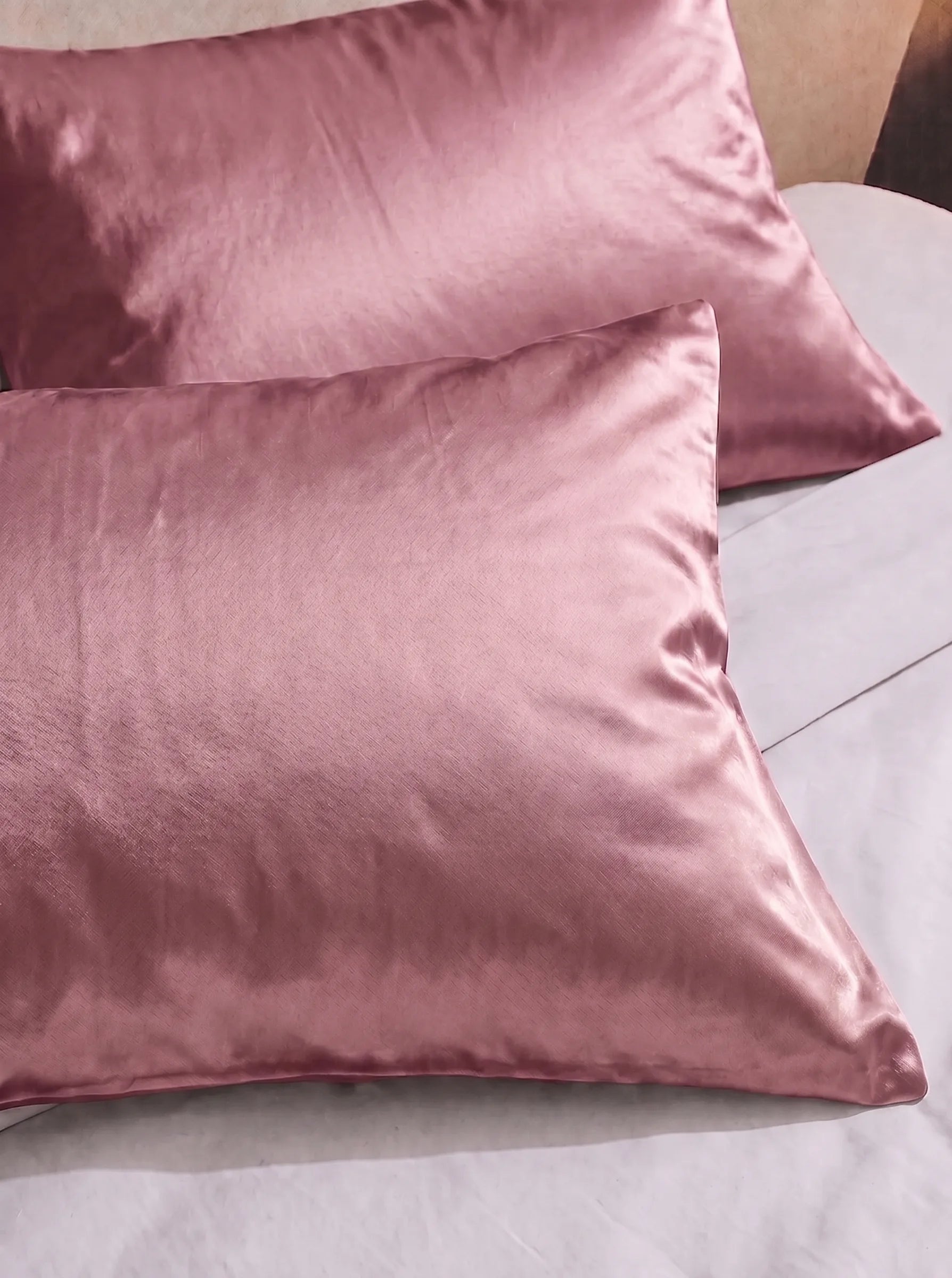 2 taie d'oreiller en soie 25 mommes rose sur lit blanc.