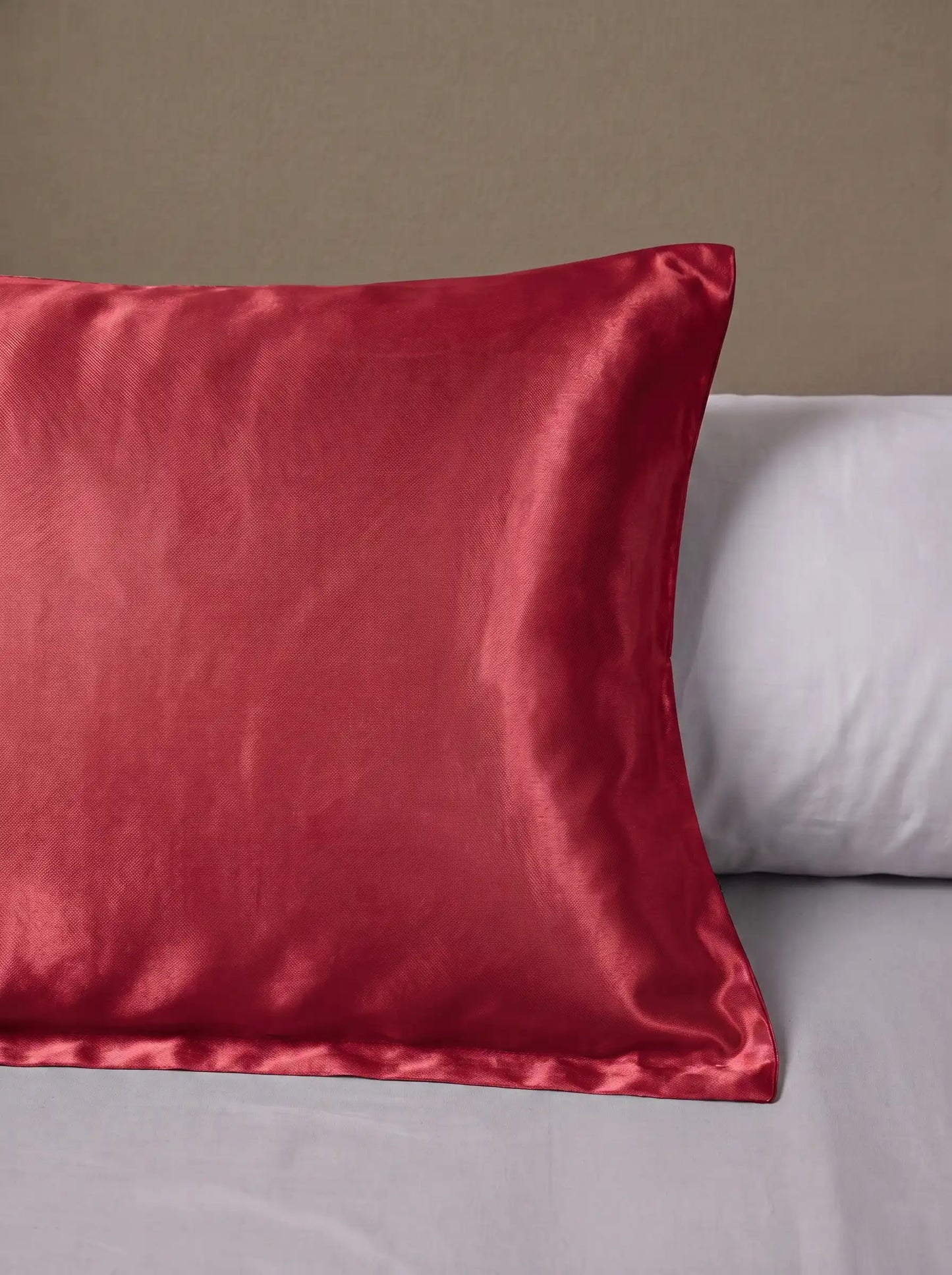 Taie d'oreiller en soie 25 mommes rouge posé sur un lit avec un oreiller blanc simple.