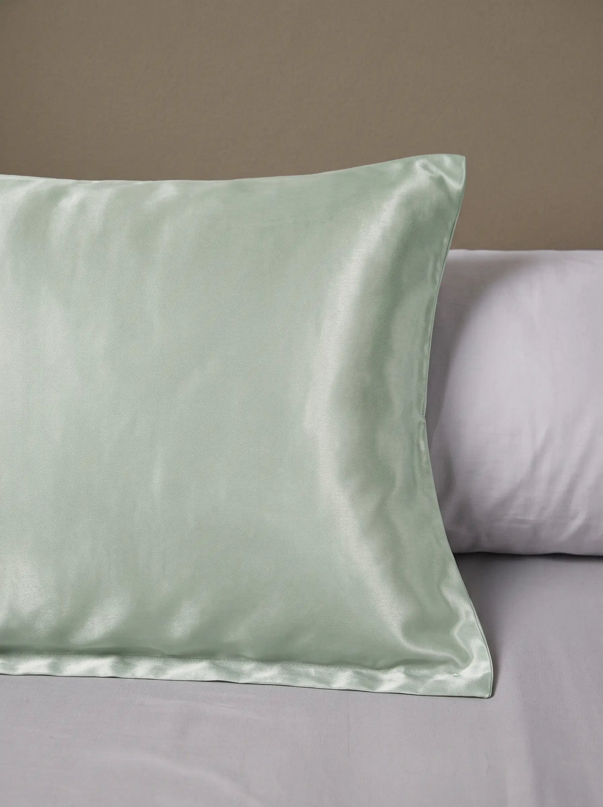 Taie d'oreiller en soie 25 mommes verte pâle posé sur un lit avec un oreiller blanc simple.