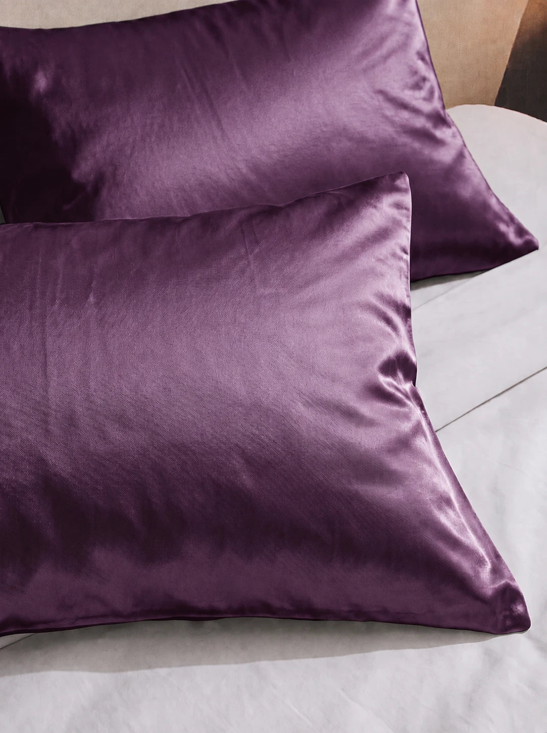2 taie d'oreiller en soie 25 mommes violette sur lit blanc.
