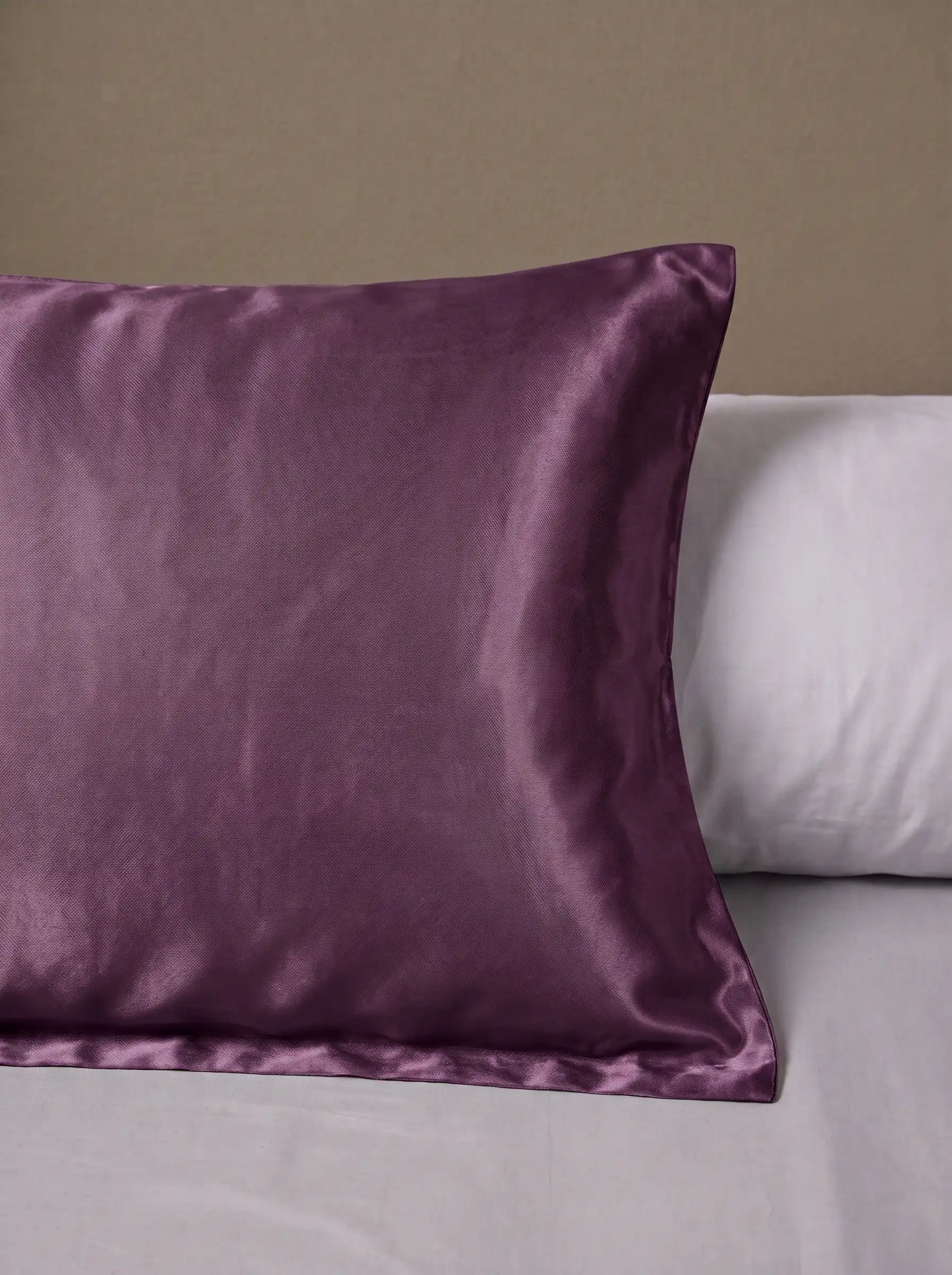 Taie d'oreiller en soie 25 mommes violette posé sur un lit avec un oreiller blanc simple.